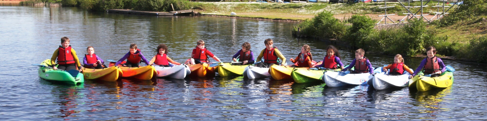 Twelve children sitting in single-sit-on-top hired Kayaks on a body of water