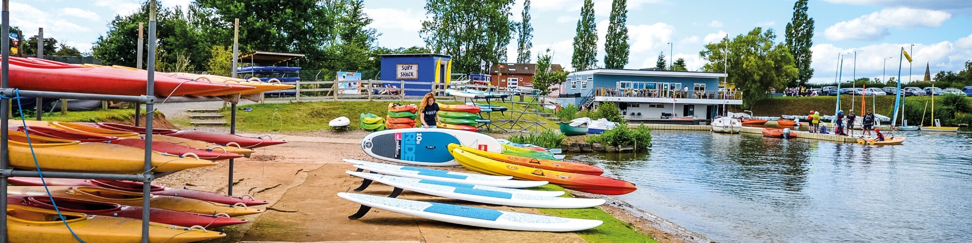 Woman organising water sports equipment on a beach next to open water