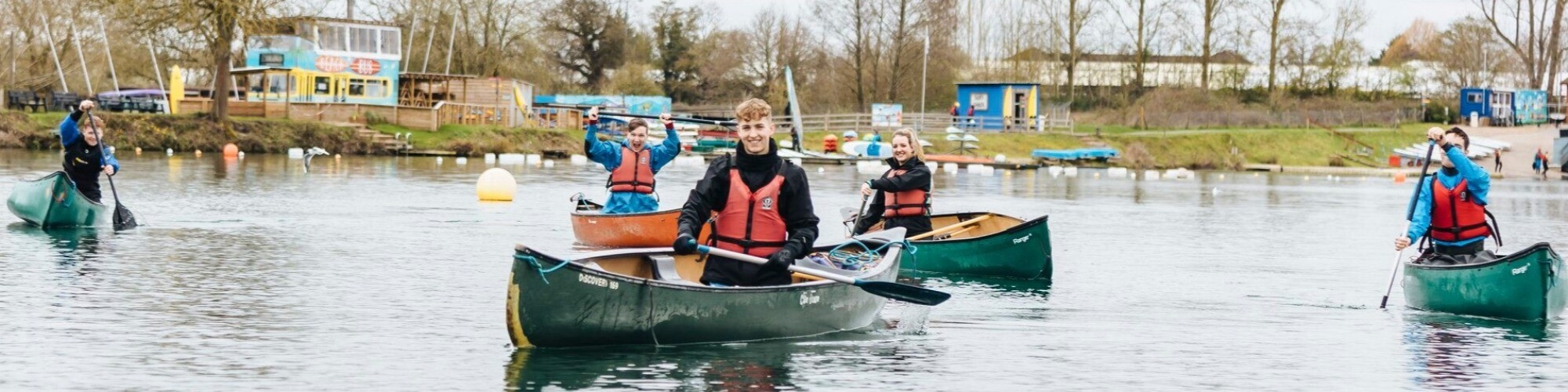 Five people launching their own open canoes on a body of water